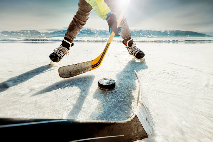 person playing pond hockey about to hit a puck in front of some mountains